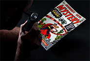 A CGC grader examines a comic book with a magnifying glass to determine its grade.